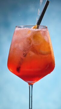 Glass of apperol spritz cocktail with orange slice and straw on blue background. Closeup of summer drink