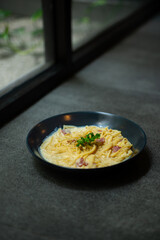 creamy smoked beef spaghetti carbonara served on black plate, over stone tile background