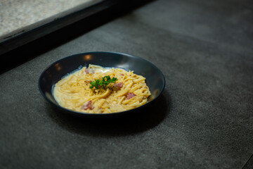 creamy smoked beef spaghetti carbonara served on black plate, over stone tile background