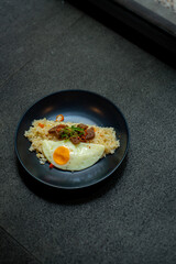 beef saikoro rice bowl and sunny side up egg on black plate, over stone tile