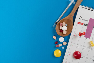 Plan to eat pills or drugs on time, with calendar on blue table background, healthy and medicine concept