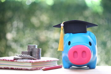 Graduation hat on piggy bank with stack of coins money on nature green background, Saving money for...