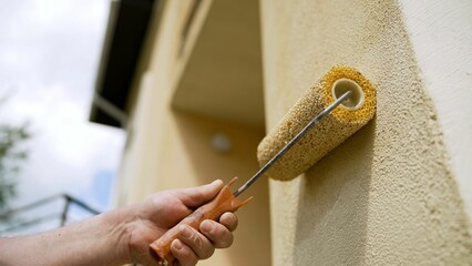 Medium shot of a wall painting, an industrial worker uses a roller and other tools to paint the...