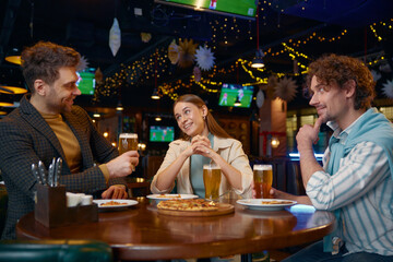Friends eating pizza drinking beer while rest in pub