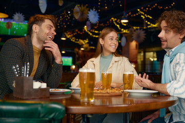 Young friends eating pizza drinking beer while rest in pub