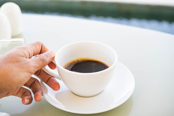 Hand holding a cup of black coffee outdoors