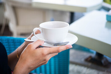Person holding a cup and saucer in an outdoor cafe