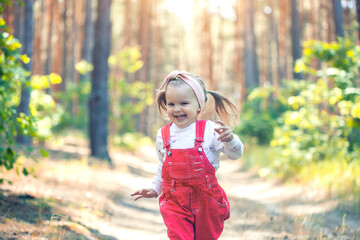 Portrait of smiling three years old caucasian child girl runs on the trail in the pine forest....