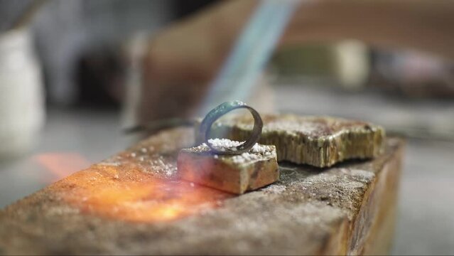 Heating with a flame jet of a metal billet of a silver ring. The work of a jeweler in the workshop