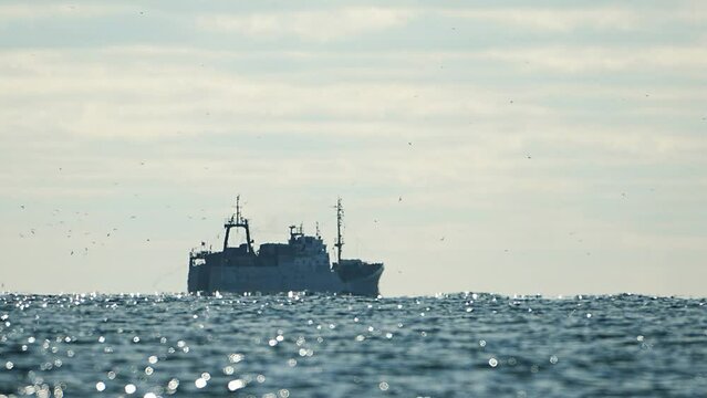 Fishing boat trawler catches fish while sailing on sea. A commercial fishing boat on the horizon in a distance sail to catch school of fish on calm sea surface in summer. Commercial catch of sea fish.