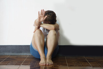 Woman sits on the floor, knees up and face down on her knees, make hand gesture to stop. Concept,...