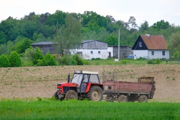 A red tractor with a trailer drives through a plowed field