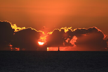 Obraz premium Sailboat silhouetted in the distance at dramatic sunset over the sea