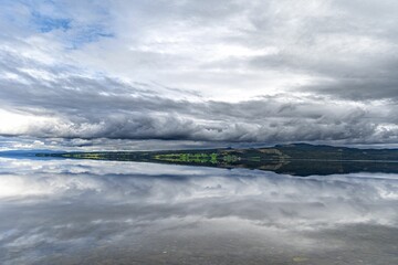 an empty lake surrounded by clouds near a forest in the distance