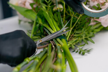 Obraz premium in a flower shop girl on a white table wraps an almost finished bouquet with adhesive tape