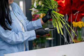 in a flower shop girl near a white table collects a flower arrangement and trims the stems