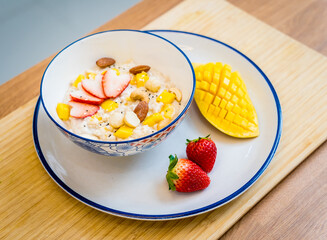 A bowl of oats with strawberries and mango arranged on a plate