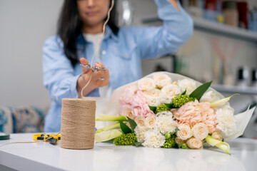 in a flower shop florist wraps a ready-made tender in a white paper wrapper and cuts off a rope...