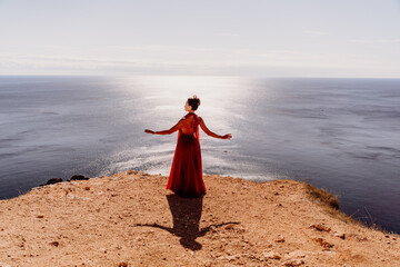 Woman red dress sea. posing on a rocky outcrop high above the sea. Girl on the nature on blue sky...