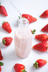 Glass bottle filled with strawberry-flavored milk surrounded by fresh strawberries
