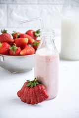 Glass bottle beside a cup filled with strawberries