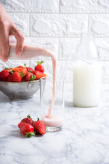Strawberry juice poured into a glass with strawberries and milk