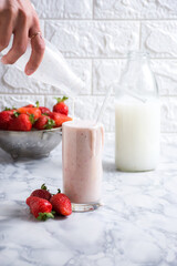White liquid from a glass onto fresh strawberries in a small bowl
