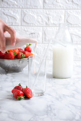 Woman pours milk over fresh strawberries on a kitchen counter