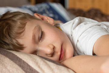 In the early morning, a boy with blond hair and freckles is fast asleep on the bed