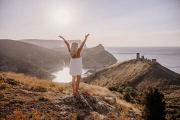 A woman is standing on a hill overlooking a body of water. She is wearing a white dress and she is happy.