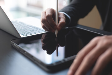 Closeup of businessman using stylus pen signing e-document on digital tablet and working on laptop...