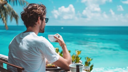 A young man is enjoying breakfast on the terrace of a tropical hotel resort, with the blue ocean or sea and clear sky in the background. - Powered by Adobe