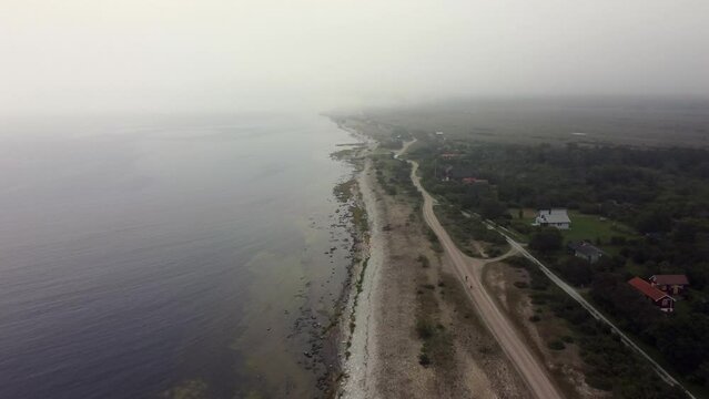 Aerial footage of a coastal road along the shoreline of Oland Island on a foggy morning, Sweden