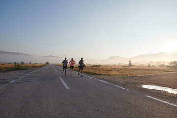 Obraz premium A group of friends, athletes, and joggers embrace the early morning hours as they run through the misty dawn, energized by the rising sun and surrounded by the tranquil beauty of nature