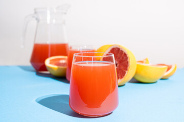 Grapefruit juice in a glass among fresh grapefruits on blue and white background
