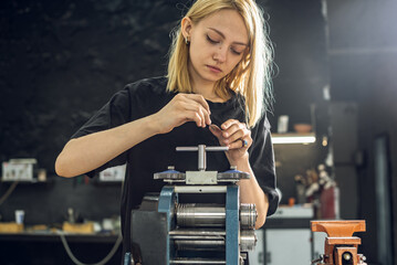 A female jeweler rolls a piece of jewelry in the form of a silver ring with a press. Craft in a...