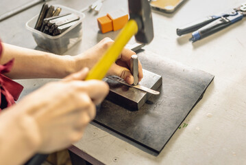 A jeweler uses a hammer to hammer out a unique ring design with a metal stamp. Craft in a jewelry workshop
