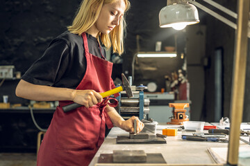 A jeweler uses a hammer to hammer out a unique ring design with a metal stamp. Craft in a jewelry workshop