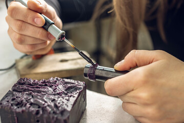 A female jeweler constructs a unique ring design using wax melting. Craft in a jewelry workshop
