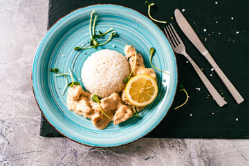 Chicken fricassee on a turquoise plate with lemon and rice on the side. Beautiful presentation of the dish.