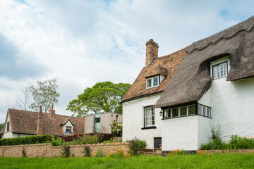 Old English thatched cottage with unusual windowed porch seen next to a more recent home with an...