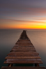 sunrise seascape with an old wooden dock leading out into the calm ocean waters