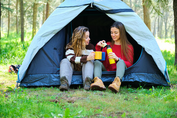 Two women sitting in a tent drinking from yellow and blue cups. Scene is relaxed and peaceful