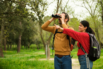 A man and a woman are looking at something in the distance with binoculars. The man is pointing at...