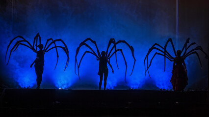 a group of figures with spider-like appendixes emerging from their backs, standing in a dimly lit space with a bluish tint.
