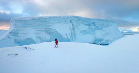 Two men ski on Antarctica snow hill glacier in sunset. Travel, active lifestyle, sport, recreation in Arctic wild nature landscape. Snow covered mountains, icy ocean, winter scene. Aerial drone flight