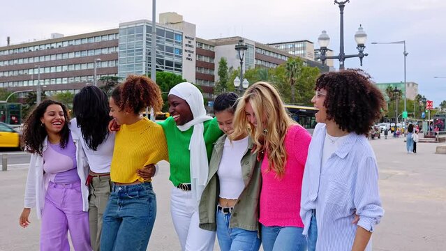 Happy diverse group of young women friends walking together outdoors. Female friendship concept with cheerful girls hugging each other showing unity and community.