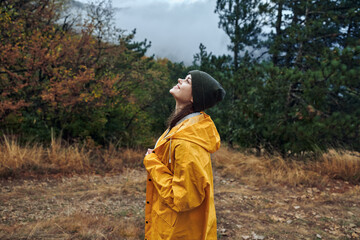 A woman wearing a yellow raincoat standing in the middle of a lush field surrounded by trees and nature