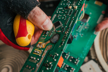 Close-up view of a hand in a red glove holding a yellow screwdriver while working on repairing an...