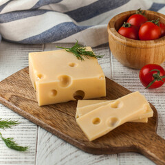 Maasdam cheese displayed on a wooden cutting board, garnished with dill and accompanied by fresh cherry tomatoes